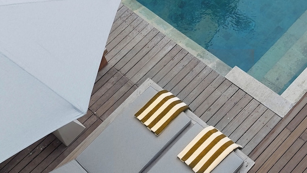 Un espace aménagé au bord de la piscine, avec deux chaises longues grises, un parasol blanc et une terrasse en bois.