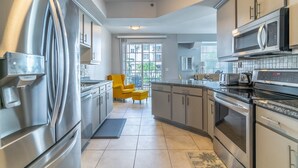 Une cuisine moderne avec des appareils en acier inoxydable, une chaise jaune et une vue à travers la porte vitrée.
