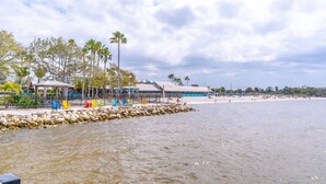 Un complexe hôtelier situé en bord de mer, doté d’une piscine, de palmiers et d’une plage.