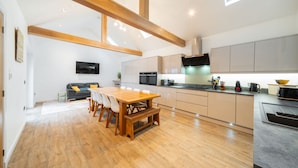 A modern kitchen with wooden beams, a dining area with a wooden table and chairs, and a flat-screen TV mounted on the wall. - The Corner House -  a house that sleeps 10 guests  in 4 bedrooms (Hopeman)