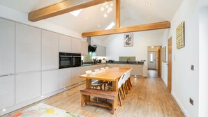 A spacious kitchen with a large wooden table and bench, white cabinets, and a skylight. - The Corner House -  a house that sleeps 10 guests  in 4 bedrooms (Hopeman)