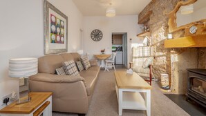 A cozy living room with a sofa, a wooden table, a clock, and a stone wall. - Cosy Garden Cottage | Fleming Place (St Andrews)