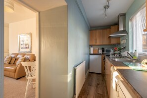 A compact kitchen with wooden cabinets, a white refrigerator, and a microwave. - Cosy Garden Cottage | Fleming Place (St Andrews)