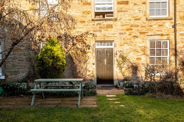 A stone building with a wooden door, a bench, and a small garden area.