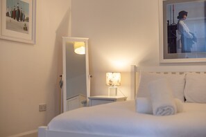Una habitación de hotel con cama, mesita de noche, lámpara, espejo y cuadros en las paredes.