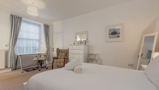 A neatly arranged bedroom with a bed, a desk, a chair, a dresser, and a mirror. - Cosy Garden Cottage | Fleming Place (St Andrews)