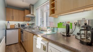 A compact kitchen with wooden cabinets, a built-in microwave, a sink, and a coffee maker. - Cosy Garden Cottage | Fleming Place (St Andrews)