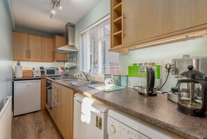 A compact kitchen with wooden cabinets, a built-in microwave, a sink, and a coffee maker. - Cosy Garden Cottage | Fleming Place (St Andrews)