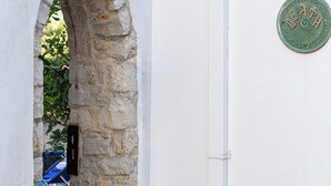 An arched stone doorway leading to a tiled interior, a metal plaque on the wall, and a white wall with a vertical pipe. - Villa Delfi /w private pool, at a serene village (Agia Triada)