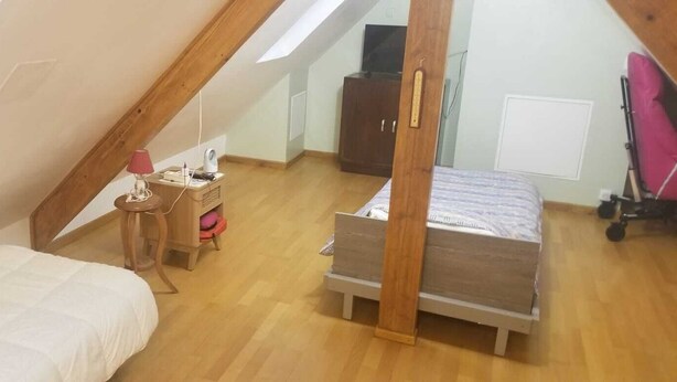 Una habitación pequeña y acogedora con techo inclinado, una cama, una mesita con lámpara y un televisor sobre un mueble.