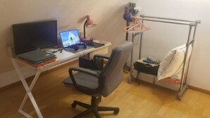 Una habitación con escritorio, silla, cama, televisor y un tendedero.
