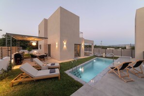 Un área de piscina moderna al aire libre con sillones de descanso, una parrilla y un porche cubierto.