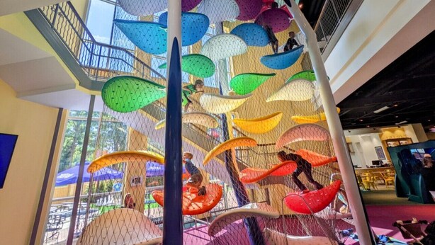 A multi-level indoor play area with colorful, netted climbing structures and slides.