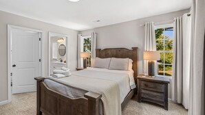 A bedroom with a large bed, bedside tables, a nightstand, a window with curtains, and a door.