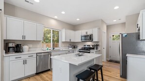 A modern kitchen with white cabinetry, stainless steel appliances, and a central island with stools.