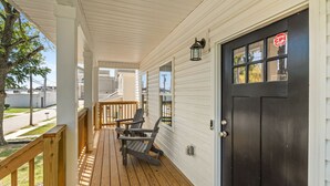 A covered porch with two Adirondack chairs, a wooden railing, and a black door with a CPI sticker.