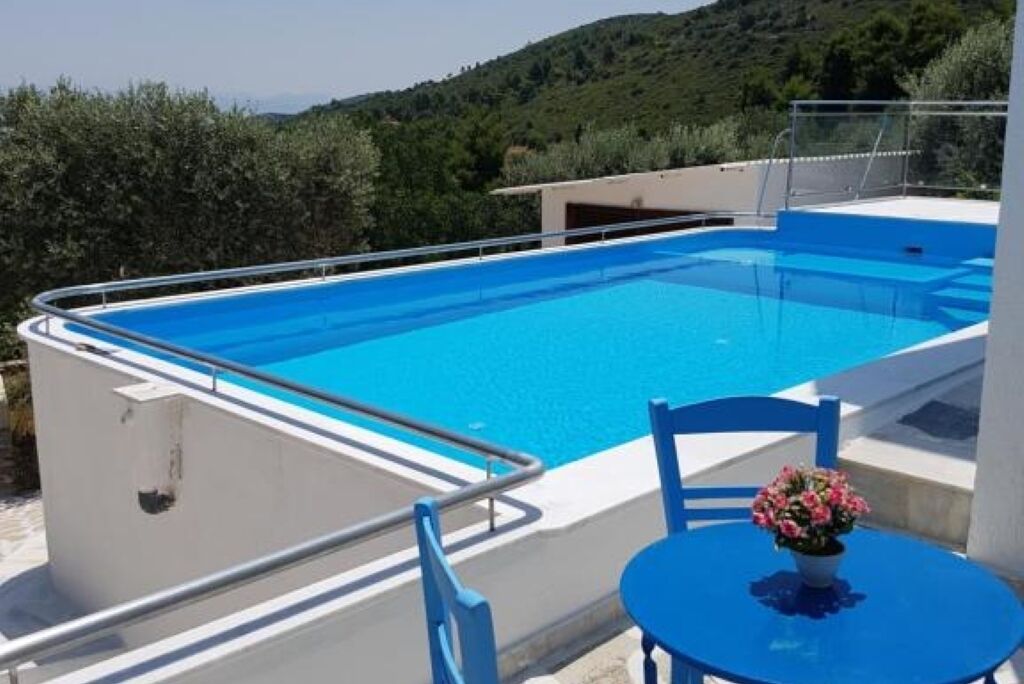 A rectangular pool with a blue interior, surrounded by a white deck and a metal railing.