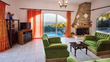 Una sala de estar con televisor, sofás verdes, chimenea y vista al mar.