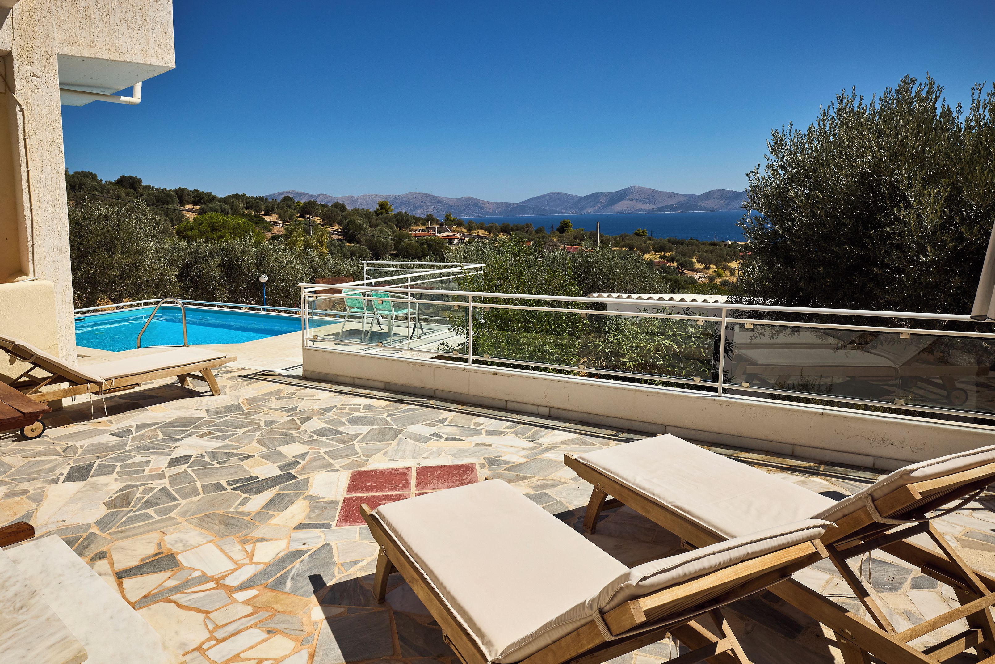 Zona de piscina con sillas de descanso y vistas al mar y a las montañas.