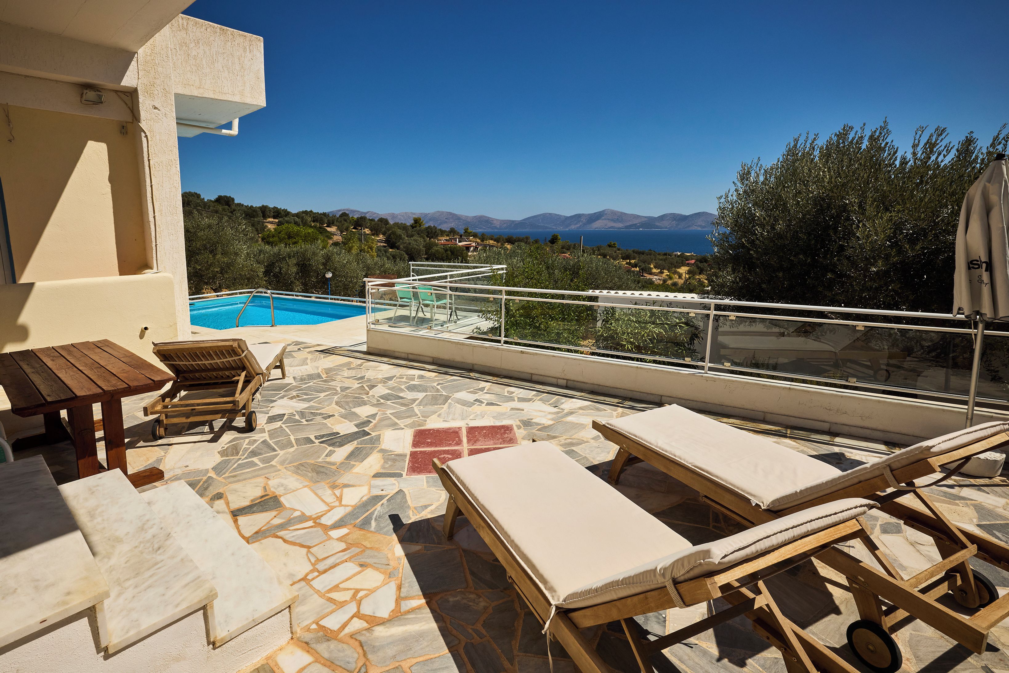 A terrace with a pool, lounge chairs, and a view of the sea and mountains.