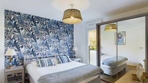 A bedroom with a large bed, a nightstand, a lamp, a woven ceiling light, a mirror, and a seahorse decoration.
