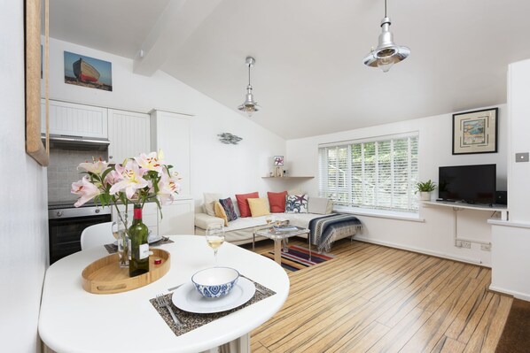 A modern kitchen with white cabinets, a dining area with a white table, and a living room with a sofa and a TV. - 3 Pentowan Court -  an apartment that sleeps 2 guests  in 1 bedroom (Carbis Bay)