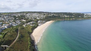An aerial view of a coastal town with a sandy beach, a railway track, and residential buildings.