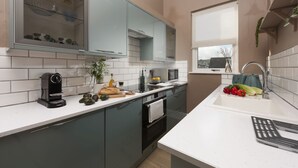 A modern kitchen with a built-in oven, a coffee machine, and a sink with fresh vegetables.