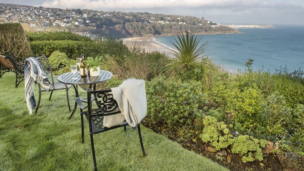 A table and chairs set on a grassy area overlooking a coastal town and the sea.