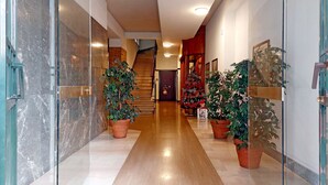 Un pasillo con pared de mármol, suelo de madera y plantas en macetas.