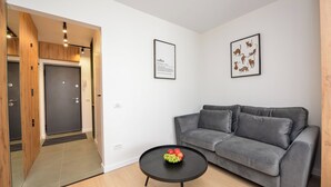 Ein modernes Wohnzimmer mit einem grauen Sofa, einem schwarzen Couchtisch mit Früchten und einem gerahmten Katzenbild an der Wand.