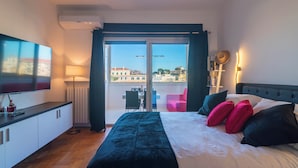A hotel room with a bed, a TV, a desk, and a balcony with a view of buildings. - Modern downtown apartment with panoramic view of St. Peter's dome (Roma)