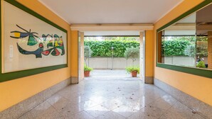 A corridor with tiled flooring, a large framed artwork on the left wall, and potted plants at the end. - Modern downtown apartment with panoramic view of St. Peter's dome (Roma)