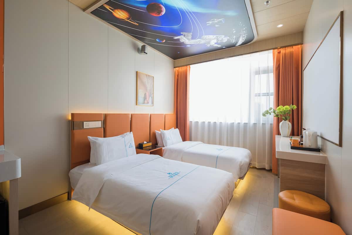 A hotel room with two beds, a desk, a mirror, and a ceiling mural.