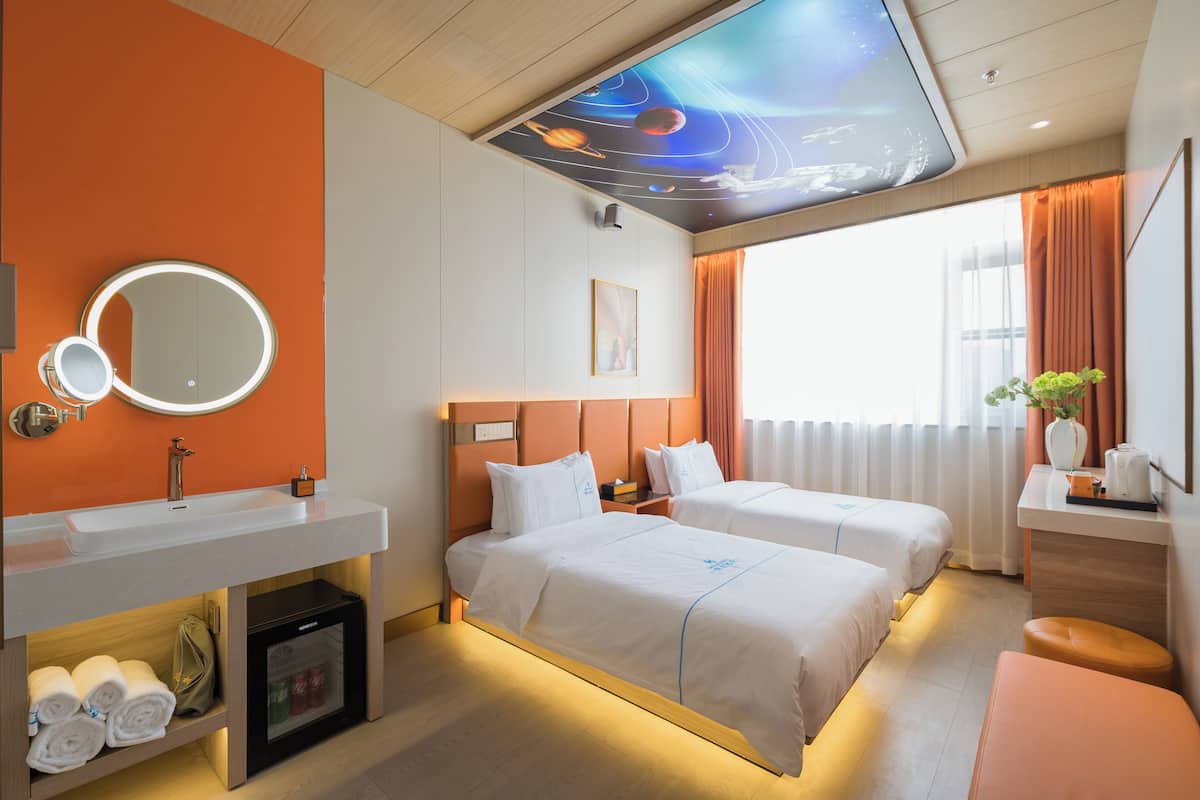 A hotel room with two beds, a round mirror, a minibar, and a ceiling mural.