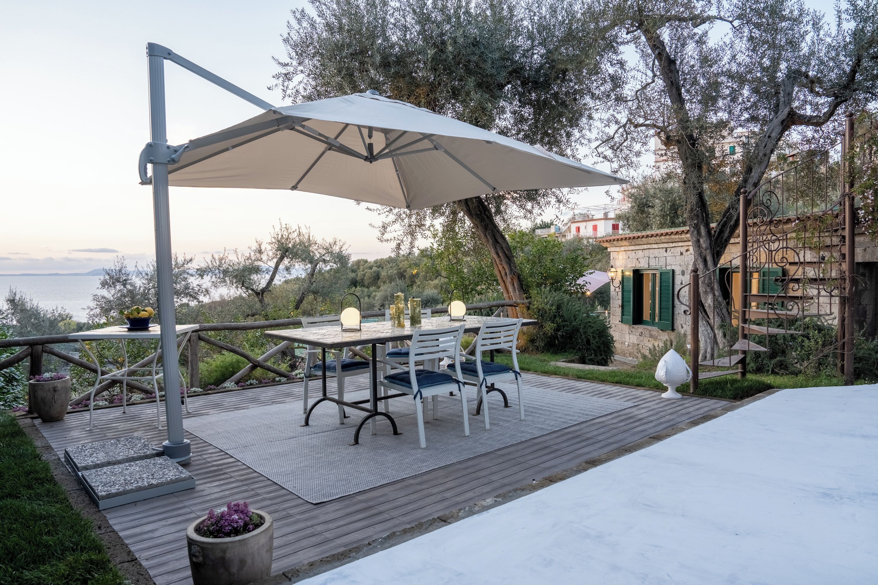 Terrassa exterior amb taula i cadires, un parasol gran i vista al mar.
