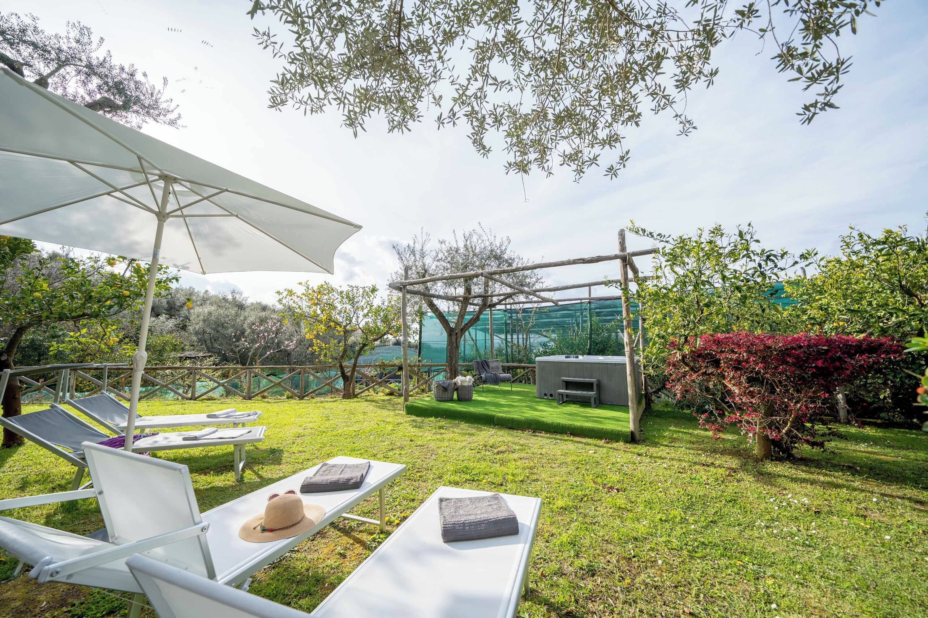 A garden with lounge chairs, a pergola, and a small outdoor kitchen area.
