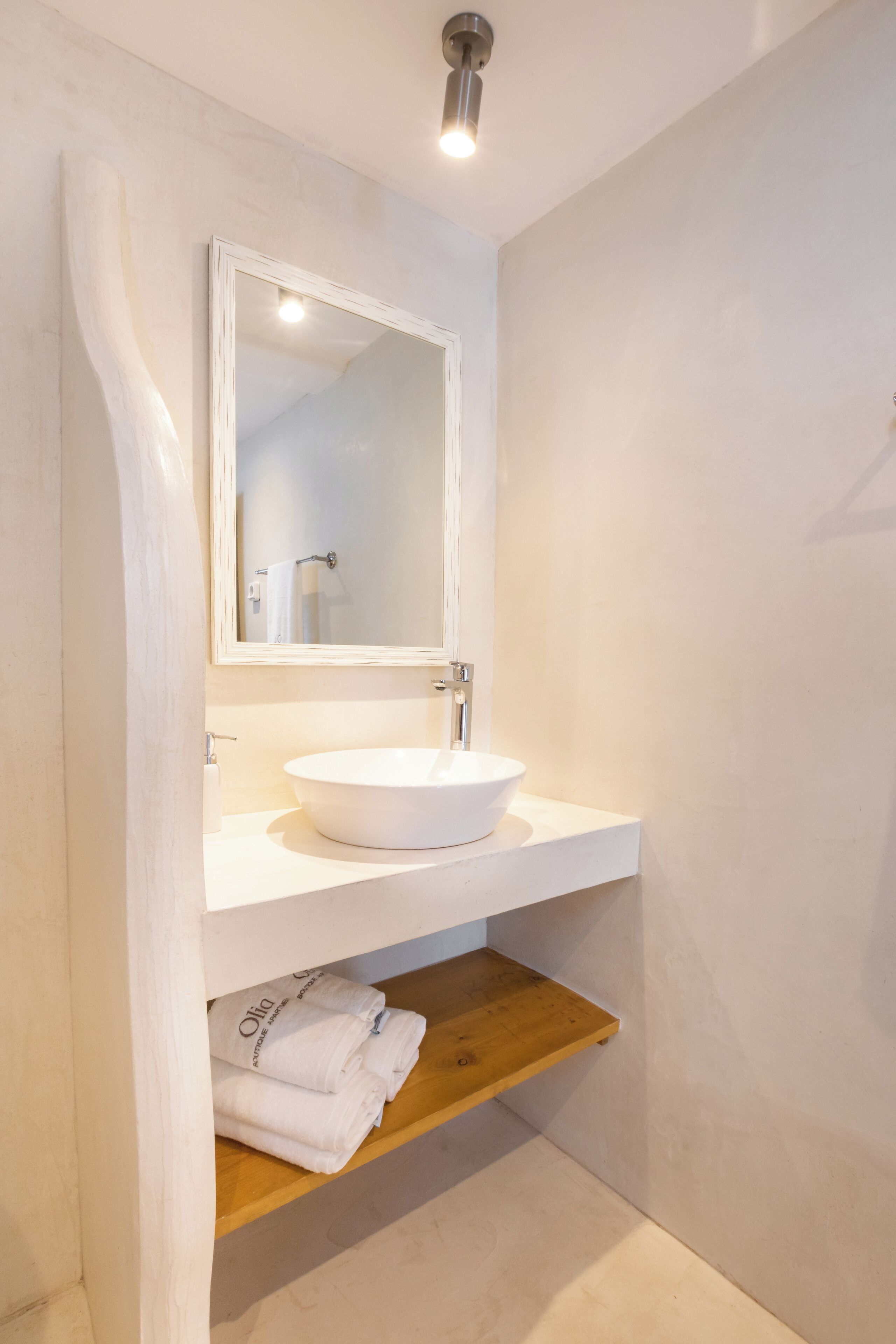 A bathroom with a white sink, a mirror, and a wooden shelf with towels.