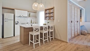 A modern kitchen with white cabinetry, a central island with bar stools, and a decorative wall shelf. - Olia Boutique Apartments (Karpathos)
