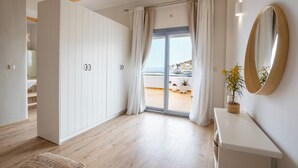 A modern room with wooden flooring, white wardrobe, sliding glass doors to a balcony, and a large mirror. - Olia Boutique Apartments (Karpathos)