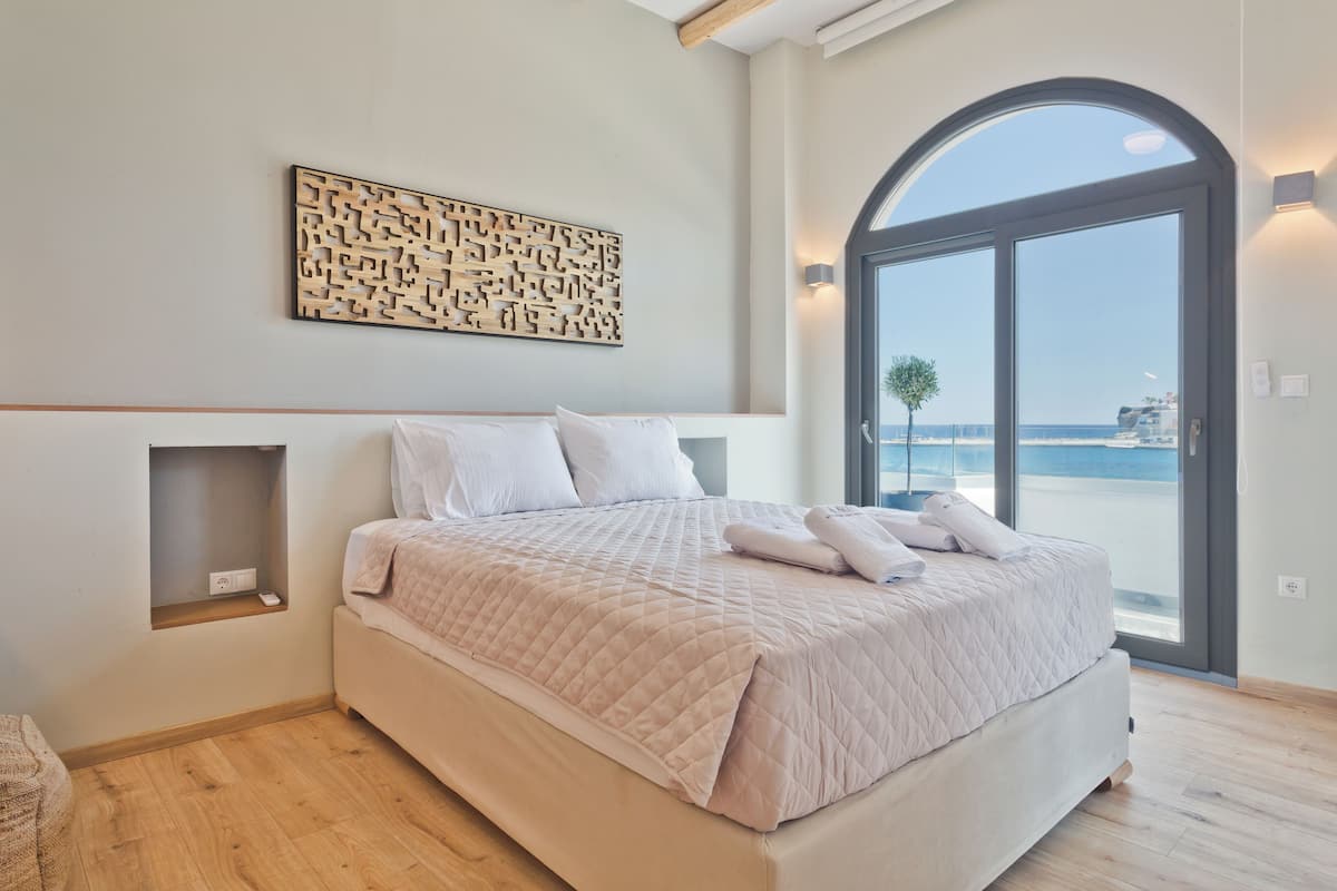A bedroom with a large bed, a built-in shelf, a decorative wall piece, and a view through a glass door.