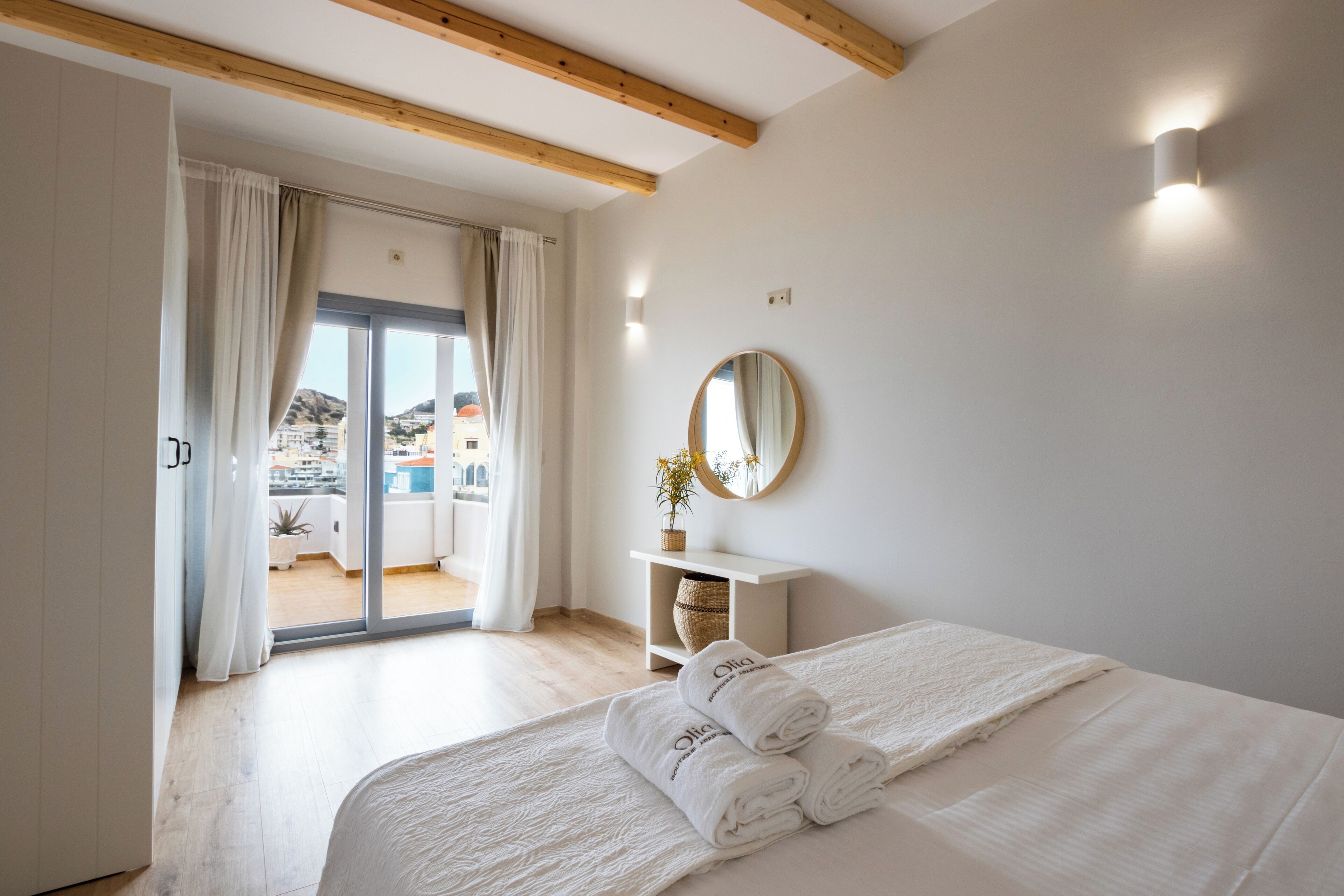 A bedroom with a large bed, a bedside table with a mirror, and a view of a balcony.