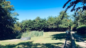 A grassy area with a wooden fence, trees, and a clear blue sky. - Sunny house close to the dunes and the sea. Families with children and dogs. (Warmenhuizen)