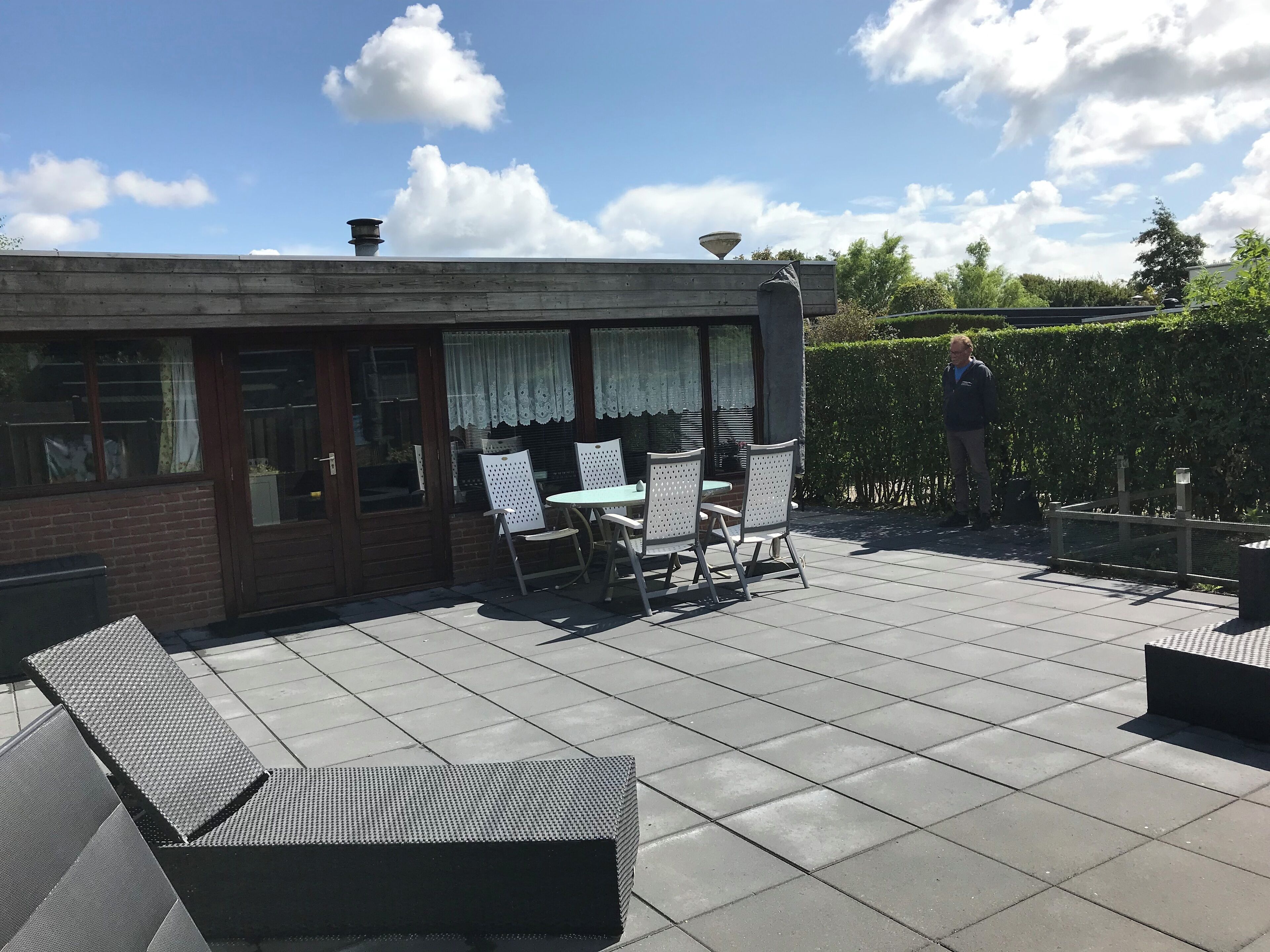 Eine Terrasse mit Tisch und Stühlen, eine Ziegelmauer und ein Hecken.