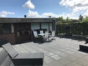 A patio with a table and chairs, a brick wall, and a hedge.