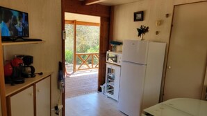 A small kitchen with a refrigerator, microwave, and a coffee maker. There is a wooden door leading to an outdoor area.