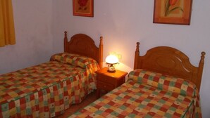 A room with two wooden beds, each with a colorful checkered bedspread. There is a nightstand with a lamp between the beds. - House El Cardón B2 in Buenavista del Norte (Buenavista del Norte)