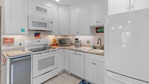 Une cuisine moderne avec des meubles blancs, un four à micro-ondes encastré, une cuisinière, un lave-vaisselle et un réfrigérateur.