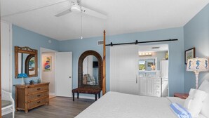 Une chambre à coucher avec un grand lit, une commode en bois, une chaise, un miroir et une porte donnant sur une salle de bain.
