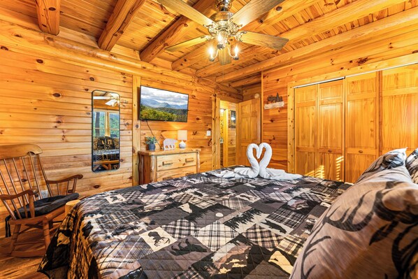 A cozy wooden cabin room with a quilted bedspread, a wooden dresser, a rocking chair, and a ceiling fan. - Peaceful Cabin with Games, Fire Pit & Hot Tub (Sevierville)
